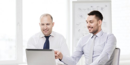 two smiling businessmen with laptop in office